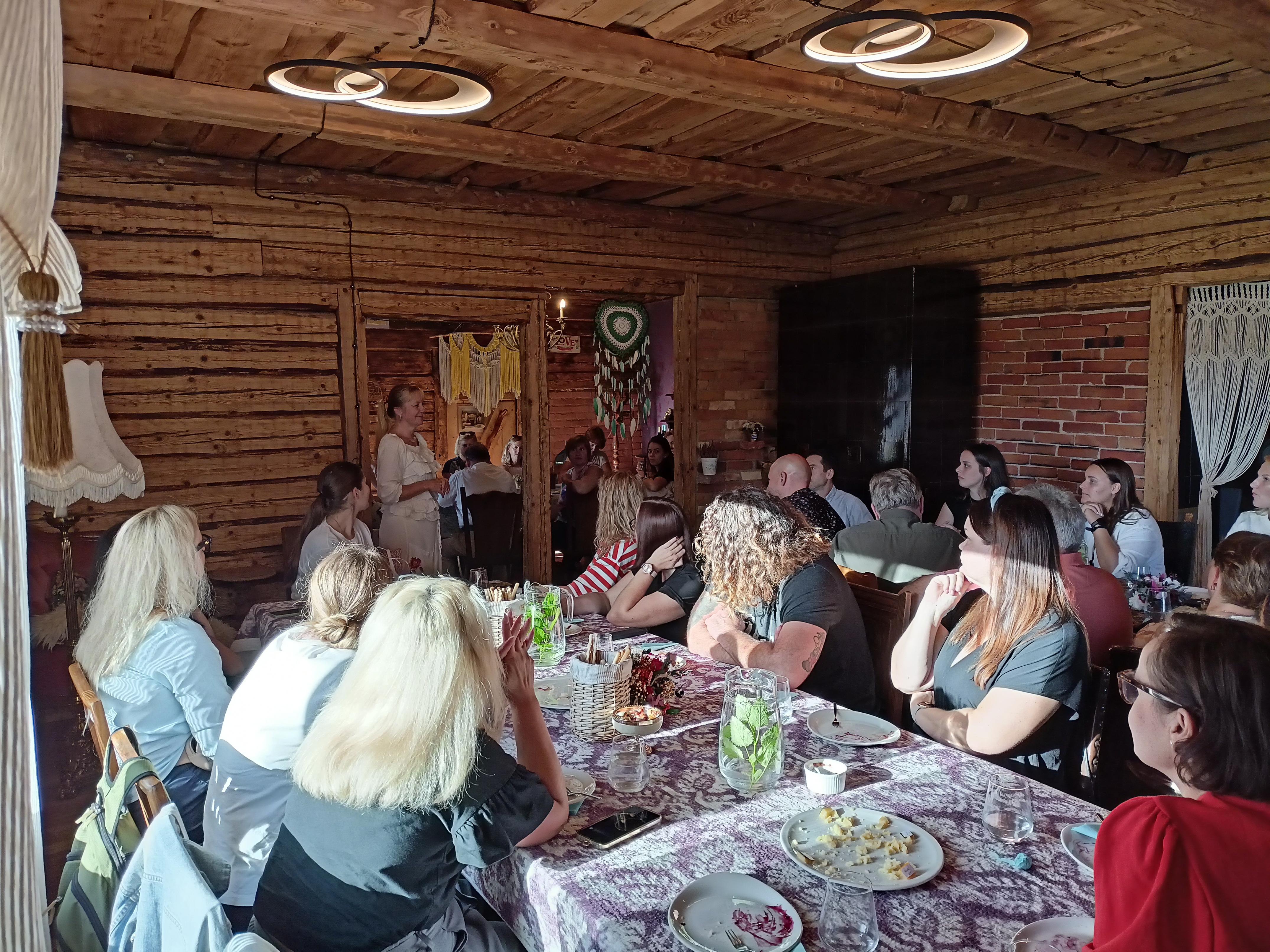 Osoby przy stołach w pomieszczeniu w domu z drewnianych bali